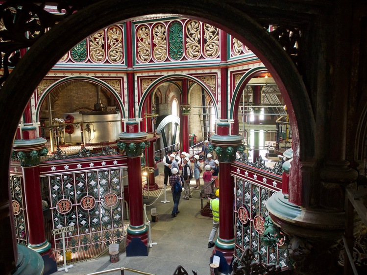 Looking down on gold, red and green metalwork adorning the top of an octagonal area. Red columns mark the octagon.
