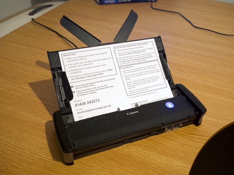 A black document-feed scanner sitting on a wooden desk.