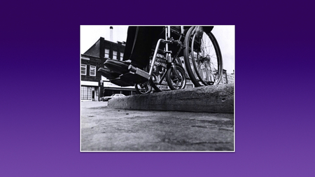 A black and white photo of a wheelchair standing at the edge of a raised curb.