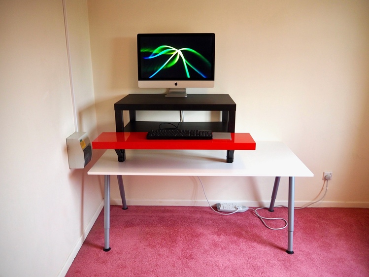 A desk with a black top, red keyboard shelf, black keyboard and an iMac.