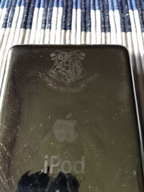 The silver back of an iPod, with some scuffs and a Hogwarts crest engraved near the top.