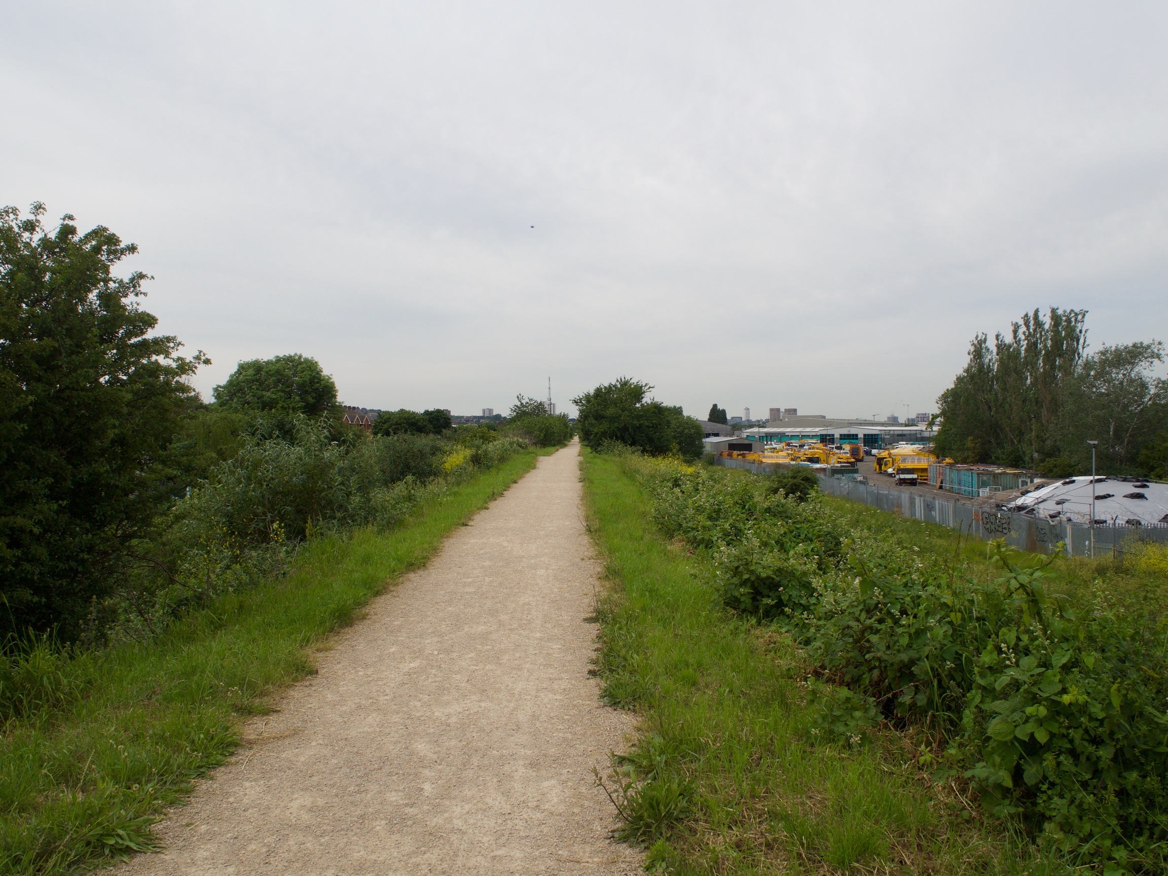 A dirt path heading forward with grass and trees on either side, and some yellow industrial machinery off to the right.