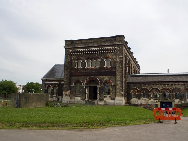 A dark brown building with rounded arches along the doors and windows, an orange safety barrier and a few bicycles.