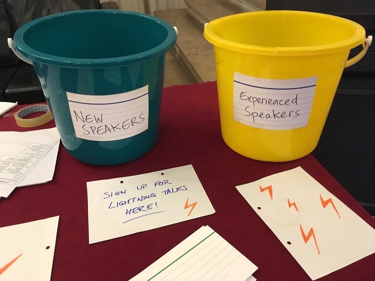 Two buckets: one green (left), labelled 'New speakers', another yellow (right), labelled 'Experienced speakers'. Below the buckets is a handwritten label 'Sign up for lightning talks here'.