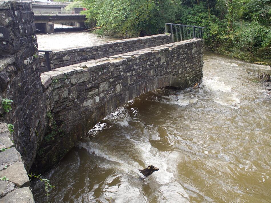 A stone bridge partially jutting out into a river.