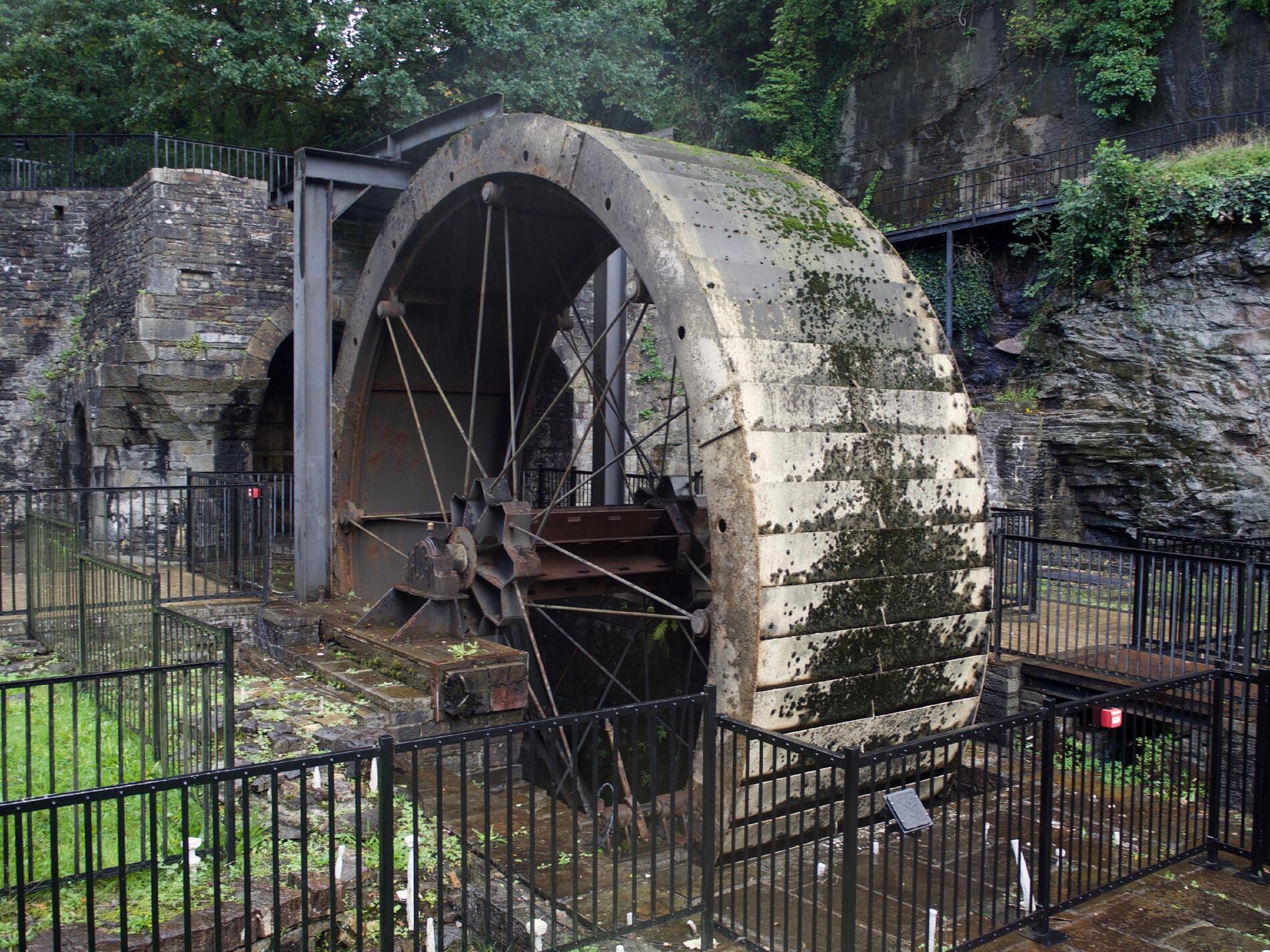 A metal waterwheel surrounded by black safety barriers.