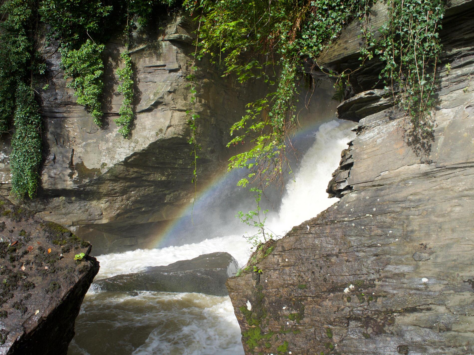White spray among rocks in the waterfall, with a rainbow between the rocks.