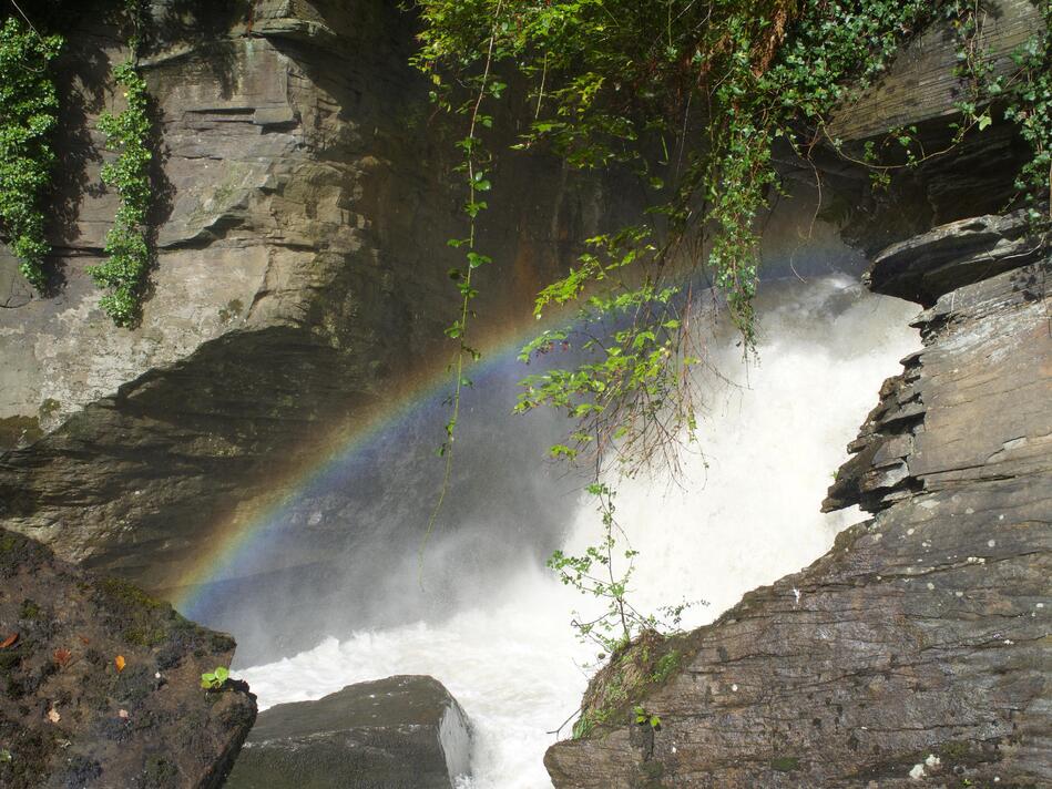 White spray from the waterfall, with a rainbow between the rocks.