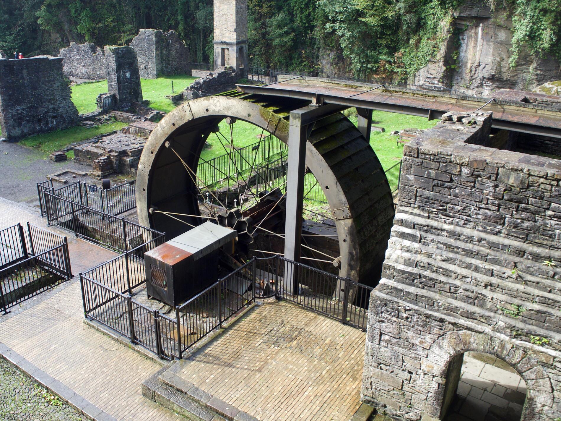 Looking down towards a waterwheel, with metal spokes and a box coming off the axle.