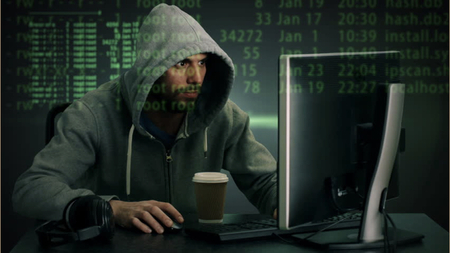 A photo of a man in a green hoodie, working at a computer with green text projected on their face.