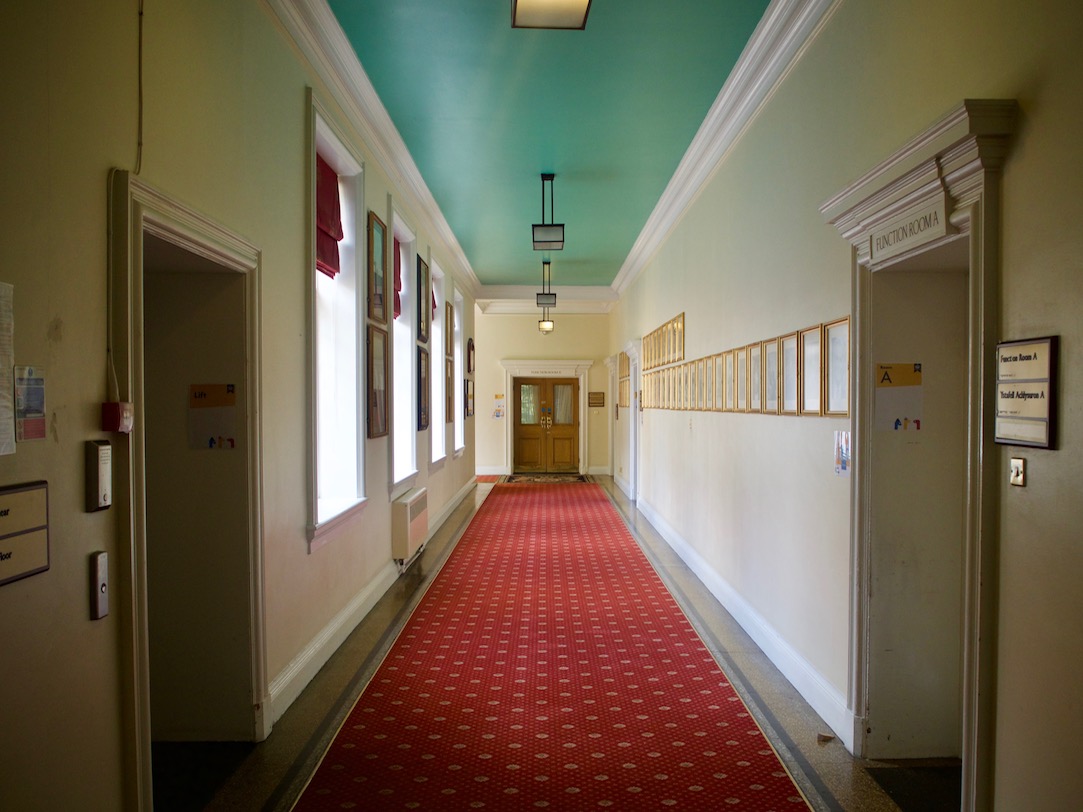 A corridor with double doors at the end, single doors on the left and right, and signs next to each of the doors.