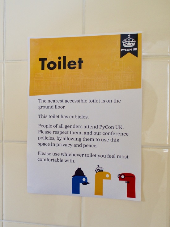 A sign on bathroom tiling with a yellow stripe at the top labelled “Toilet”.