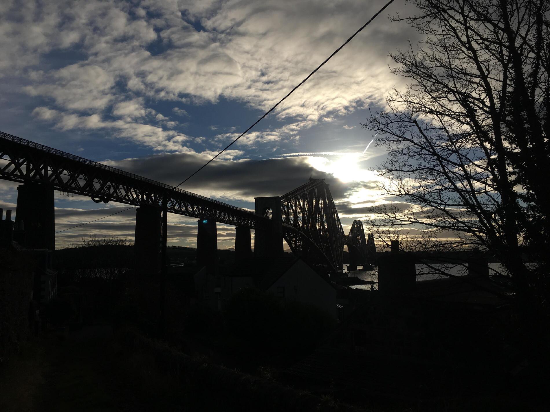 A silhouette of the bridge and some trees against a grey sky.