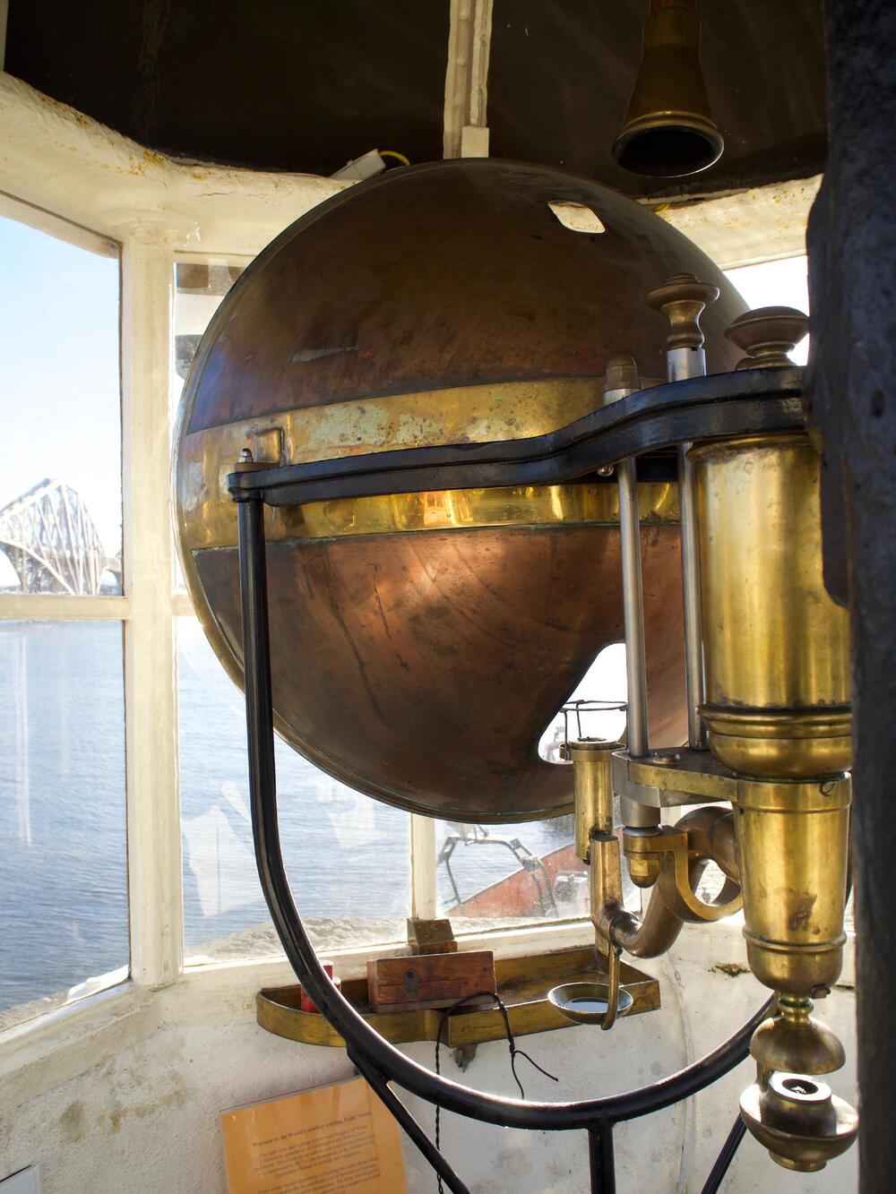 The back of a copper-coloured, parabolic lens looking out through a lighthouse window.
