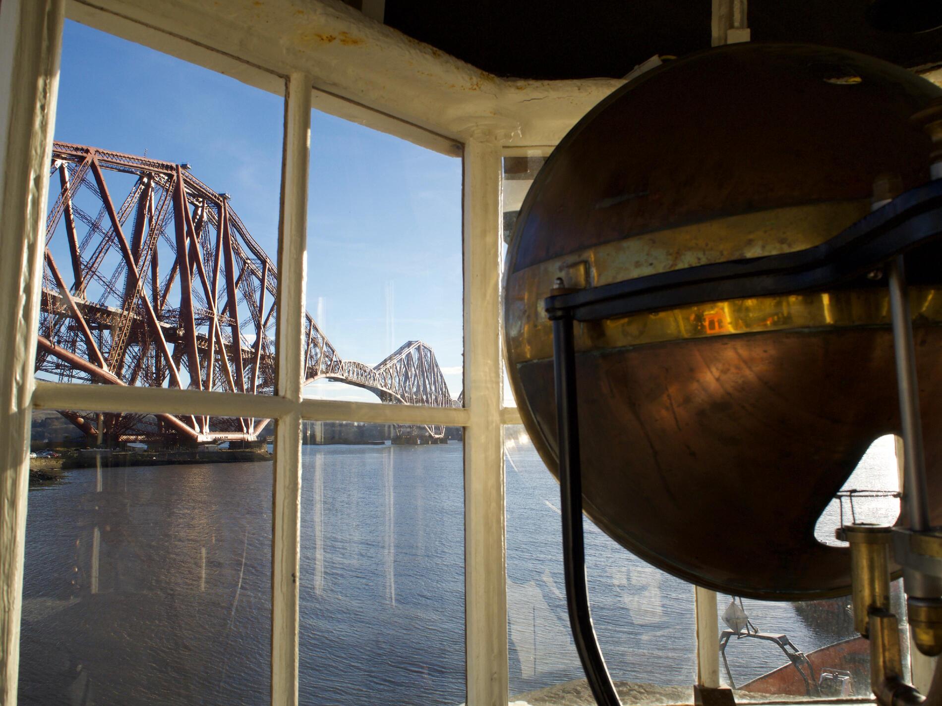 Looking from inside the lighthouse window, with a red bridge visible outside and part of a copper-coloured lamp housing inside.