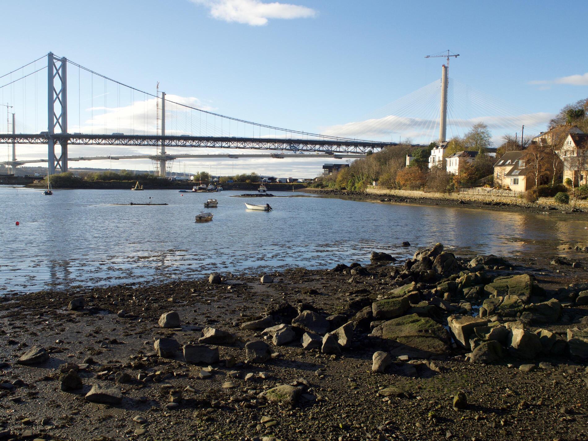 Photo from the water's edge, with two bridges in the background and a couple of boats in the water.