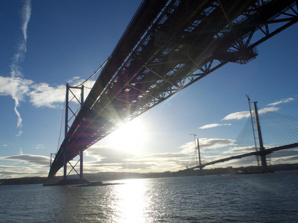 Looking at the underside of two bridges in silhouette, with lens flare in the middle of the photo.