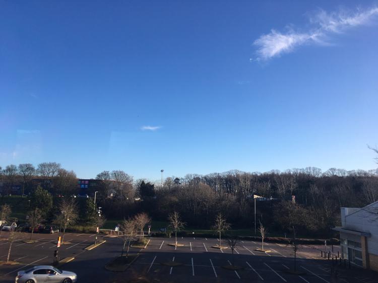 Blue sky with a handful of clouds above a car park.