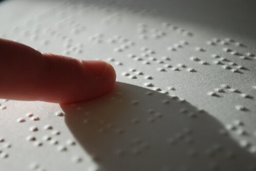 A finger feeling raised dots on a printed page of braille.