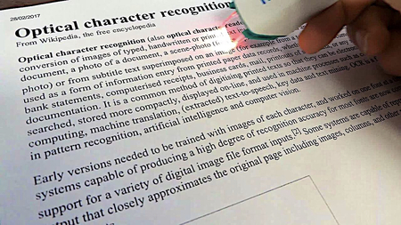 A printed page titled “Optical character recognition”, being scanned with a handheld OCR scanner with a red light.