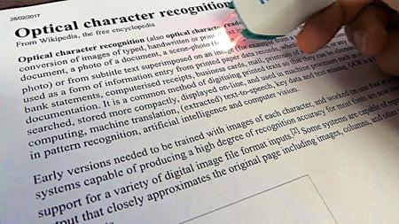 A printed page titled “Optical character recognition”, being scanned with a handheld OCR scanner with a red light.