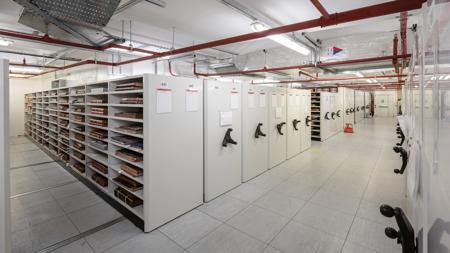 A room with a row of shelves, with the spines of some large books visible on the nearest shelves.