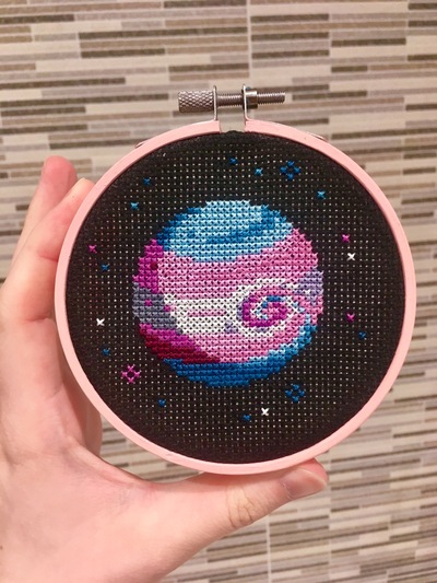 A pink embroidery hoop with a Jupiter-like planet with blue, pink and white stripes.