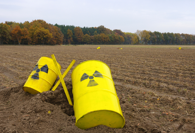 Yellow barrels with radiation warning signs lying in a field.