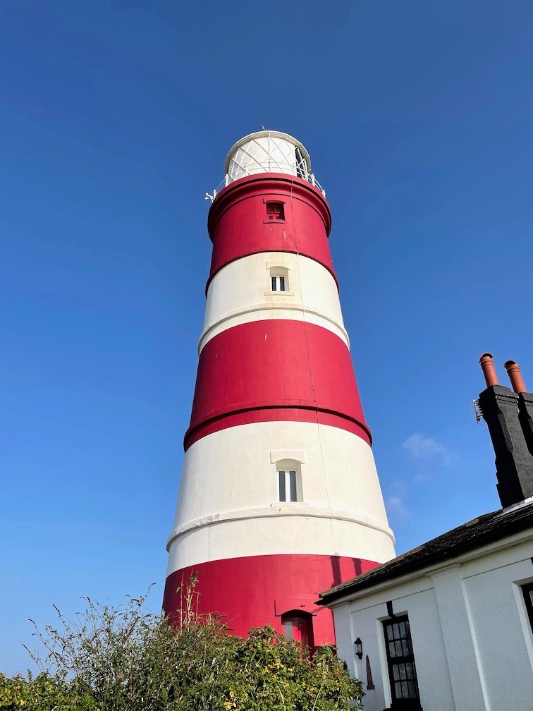 A photo of a red and white lighthouse set against a blue sky.