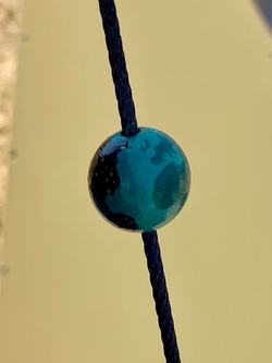 A close-up of the model of the Earth on a string. The Earth is only slightly wider than the string itself. It's a painted marble with blue-green countries on one side (including the UK), and black countries with gold dots on the other (representing cities lighting up at night).