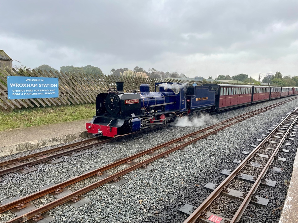 One more photo of the dark blue engine pulling a line of carriages, next to the sign for Wroxham Station.