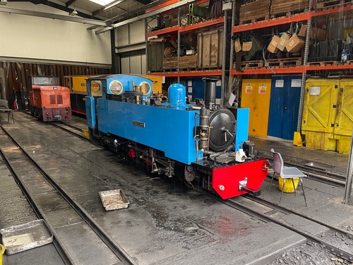 A light blue steam engine sitting in a workshop. It’s a similar shape to the first engine – fairly box like. It doesn’t have any gold decorations, just a small nameplate in the centre of the side. Around it are various boxes and tools, presumably used for maintaining the engines.