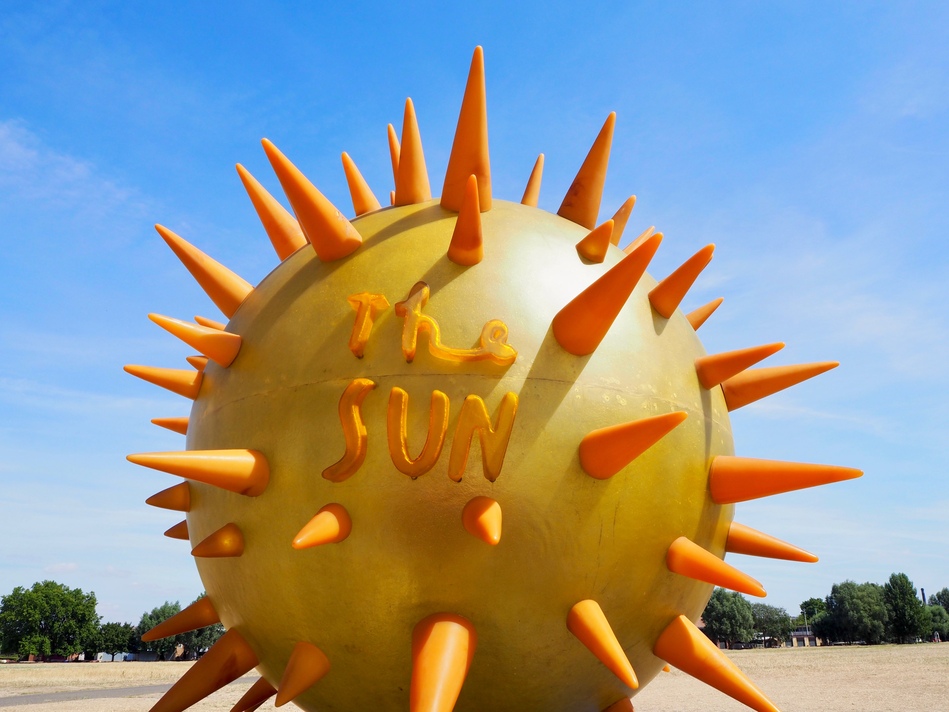 A large yellow globe with conical orange spikes. It says 'the Sun' in a handwritten font, and stands resplendent against a clear blue sky.