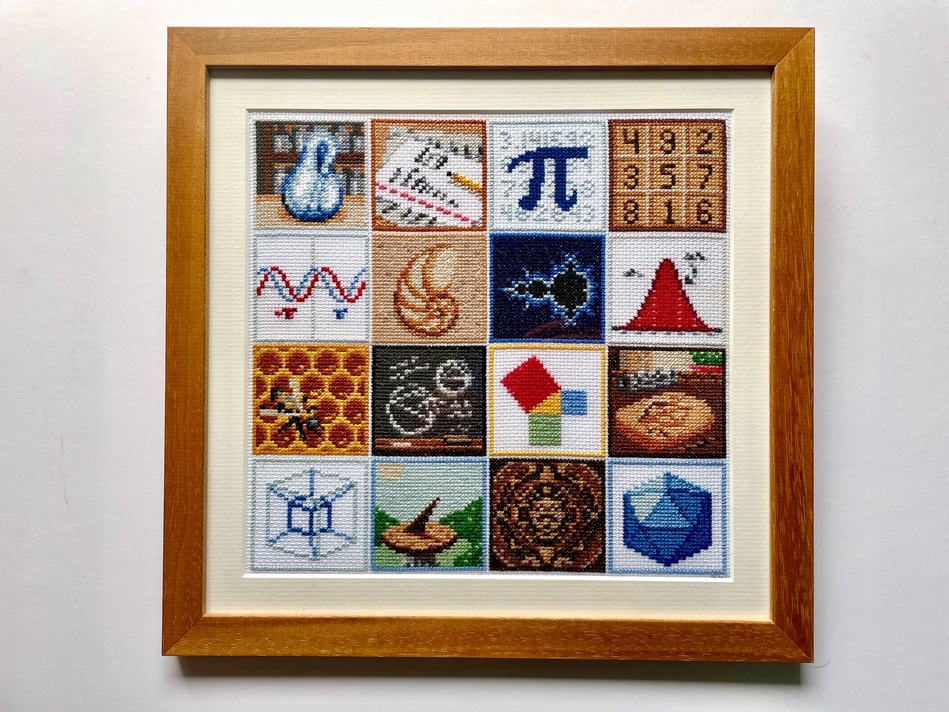 A wodden frame around a cross-stitch picture. The picture is sixteen brightly-coloured squares, arranged in a four-by-four grid. Each square has a different mathematically-related symbol, including a Klein bottle, the digits of pi, a chalkboard, and a sine wave.
