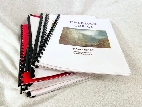 A stack of comb-bound documents, each with red card covers on one side. The cover of the topmost document says 'Cheddar Gorge' with my name and a picture.