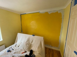 Another angle of the feature wall, which has some masking tape around it and some initial roller work for the darker yellow. The yellow doesn't fully cover the wall yet; underneath it you can see the white primer I applied to lighten the grey.
