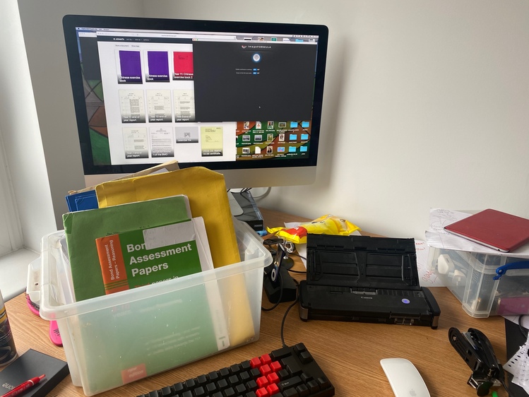 A photo of my scanning setup. I have a plastic box full of exercise books and papers, and next to it a small document-feed scanner. Behind them both is a big monitor, which has the scanning software and some of the already-scanned documents onscreen.