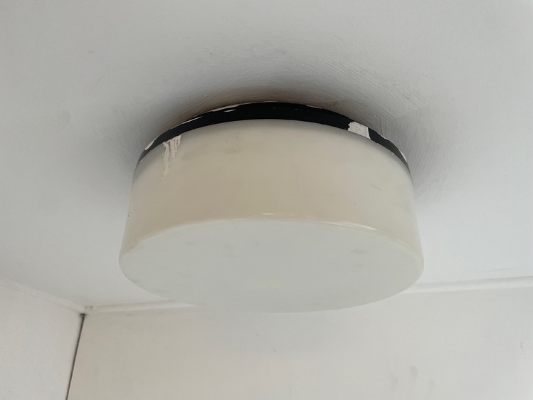 A light attached to a white ceiling. The light is a wide, stumpy cylinder made of plastic -- most of it is white, and then there's a small black base where it attaches to the ceiling.