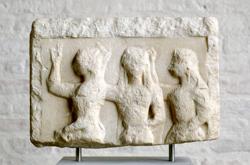 A stone relief with a rough outline of three women standing in a line and raising their hands in the same direction.