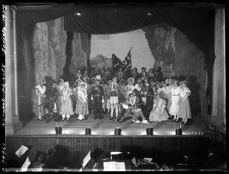 Black-and-white photo of a theatrical stage full of actors in various costumes.