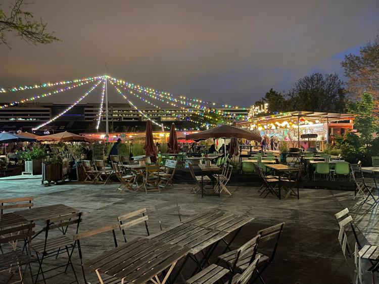 An outdoor seating area, with open-air markets visible in the background, with bright and colourful lights.