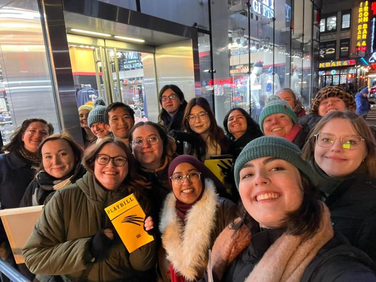 A group selfie, with people wrapped up warm in front of a New York shop, smiling at the camera and clutching Mincemeat yellow playbills.