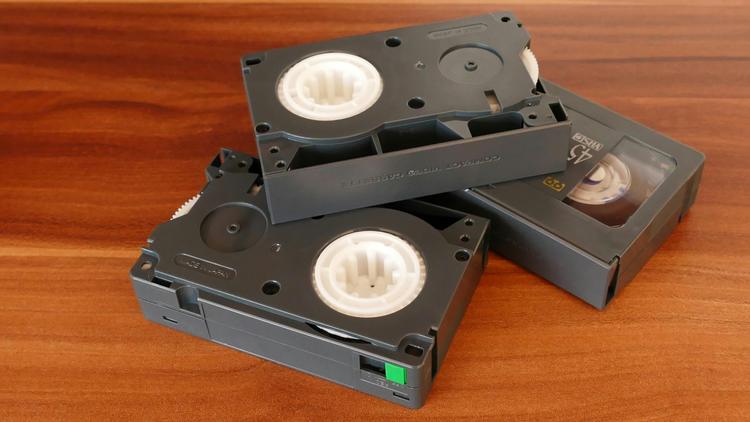 A pile of three black video cassette tapes stacked on a wooden table.