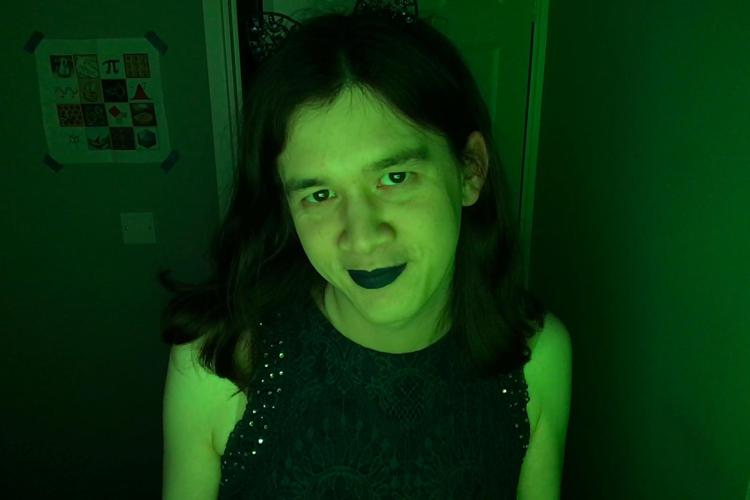 A picture of me smiling at the camera from inside my office. The room is lit up in a moody green, I have dark lipstick and a dark dress, and some cat ears vaguely visible. I am absolutely beaming with joy.