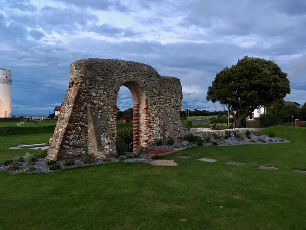 The ruin of a building, with a doorway still standing and visible. There's a tended garden around it, and a white lighthouse tower just enters the right of the frame.