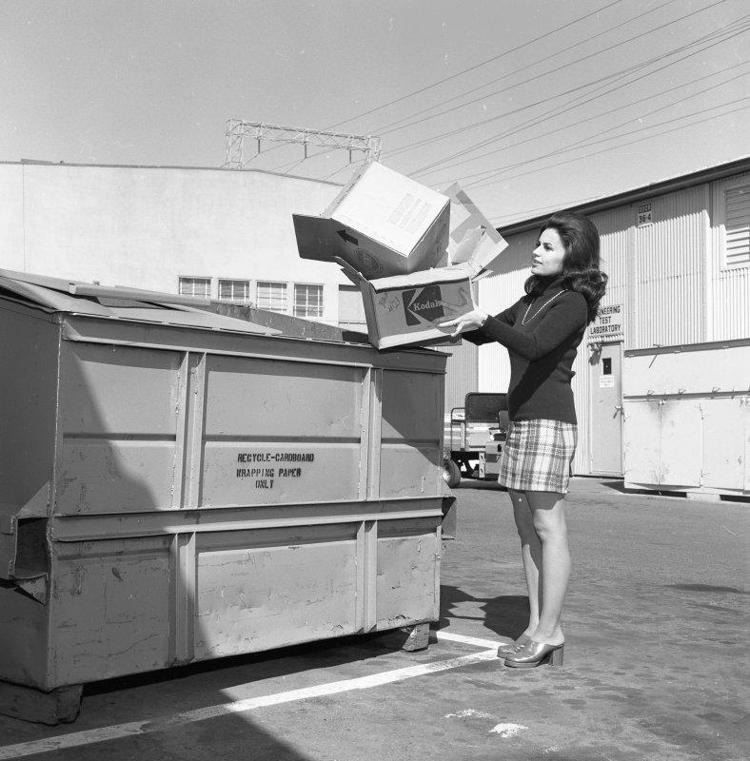 A woman putting a pile of boxes in a large bin.