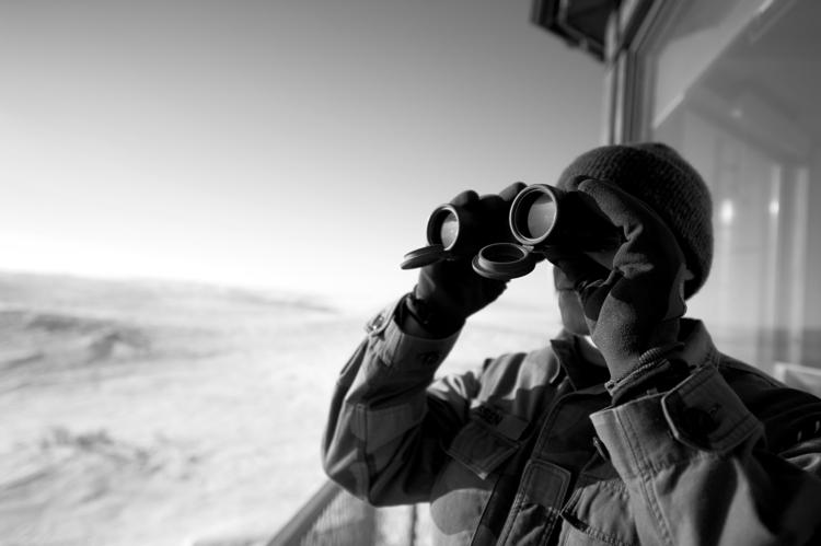 A person looks through a pair of binoculars over a snowy landscape.