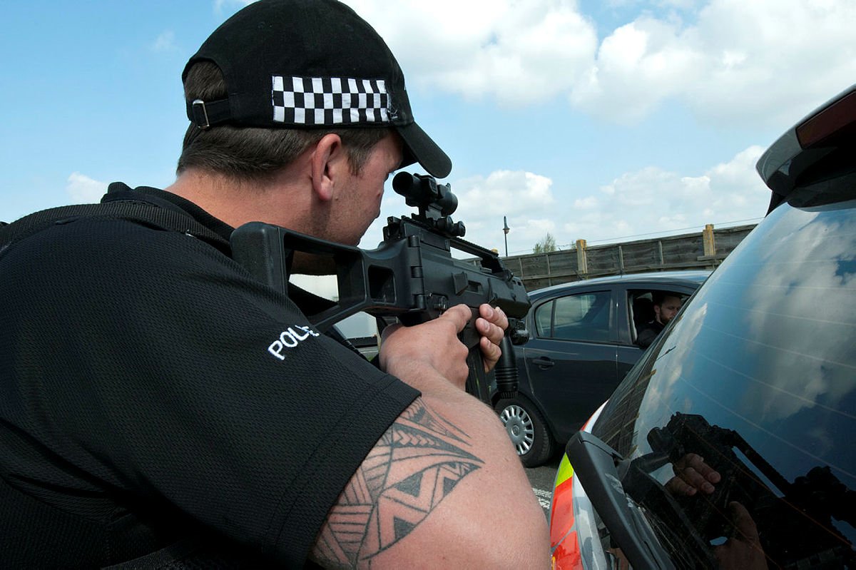 Looking from behind a police officer who is pointing a gun towards the occupant of a car.