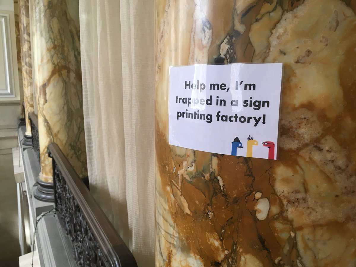 A sign on a column labelled “Help me, I’m trapped in a sign printing factory!”.