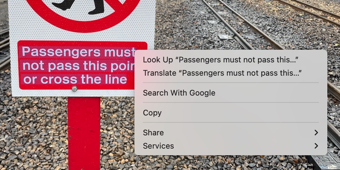 A picture of a railway sign with the text highlighted, and a popover menu offering several options: ‘Look up “Passengers must not pass this point or cross the line”’, ‘Translate “Passengers must not pass this point or cross the line”’, Search with Google, Copy, or Share.